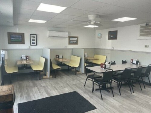 A cozy diner interior with yellow booths, tables, and black chairs, featuring a light-colored floor and wall decor.