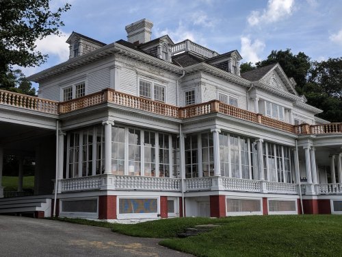 A large, elegant white mansion with multiple balconies and large windows, set against a green landscape.