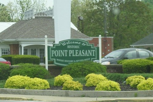 Welcome sign for Historic Point Pleasant, featuring greenery and a building in the background.