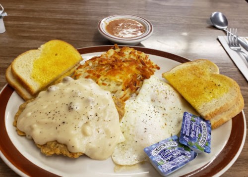A plate of breakfast featuring fried chicken with gravy, two eggs, hash browns, toast, and jelly packets.