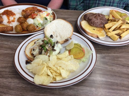 A plate with a sandwich, chips, pickles, and a side salad, alongside a burger and fries on another plate.