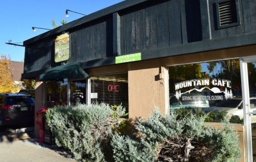 Exterior of Mountain Cafe with an "OPEN" sign, surrounded by shrubs and trees on a sunny day.