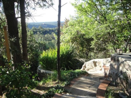 A winding stone path leads through lush greenery, with a scenic view of hills in the background.