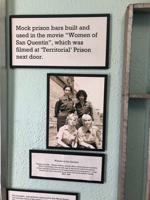 Black and white photo of four women in uniforms, with a sign about the film "Women of San Quentin" nearby.