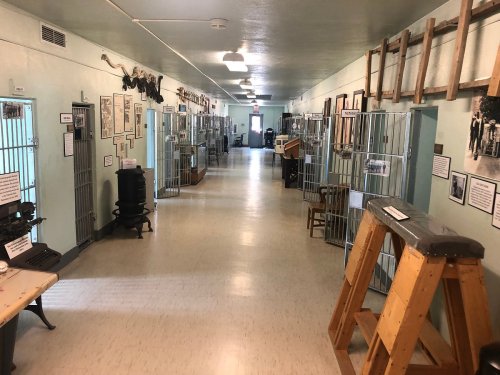 A long hallway in a museum featuring old jail cells, historical photos, and artifacts on display.