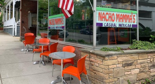 Exterior of Nacho Mamma's restaurant with orange chairs and tables, featuring a large sign for casual Mexican dining.