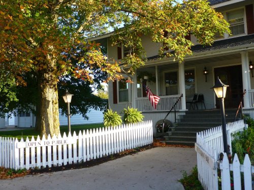 A charming house with a white picket fence, autumn leaves, and an "Open to Public" sign in front.