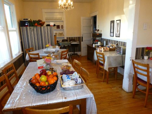 A cozy dining room with wooden floors, tables set with tablecloths, and a variety of fruits and snacks displayed.
