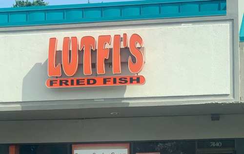 Sign for Lutfi's Fried Fish, featuring bold orange letters on a light-colored background.