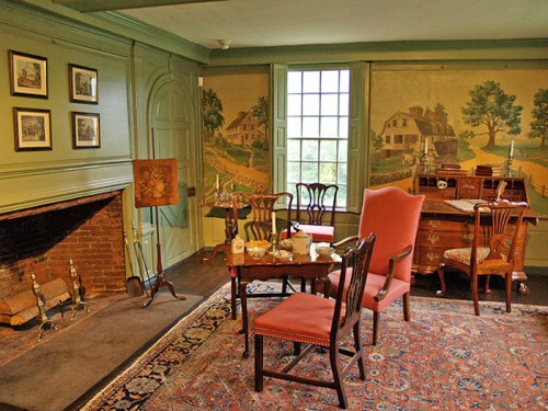 A cozy room with a fireplace, vintage furniture, and scenic wall murals depicting countryside landscapes.