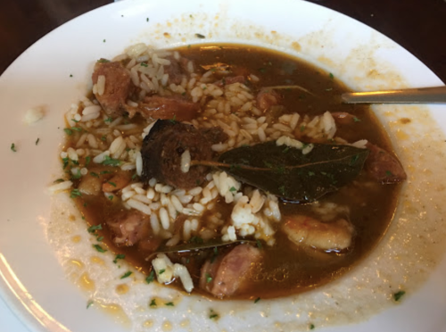 A bowl of rice and sausage stew, garnished with bay leaves and herbs, served in a white dish.