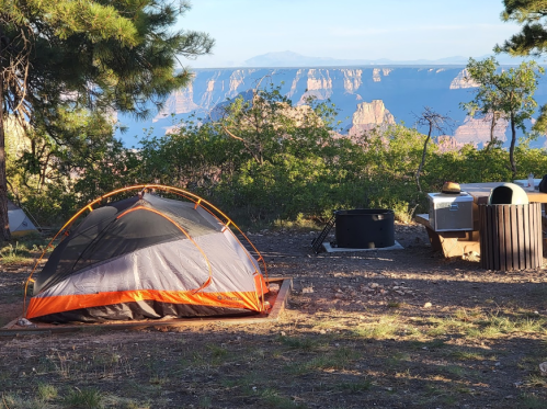 A tent set up in a campsite with a scenic view of cliffs and mountains in the background, surrounded by trees.