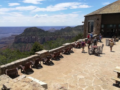 A scenic view from a stone terrace overlooking a canyon, with people sitting and walking around.