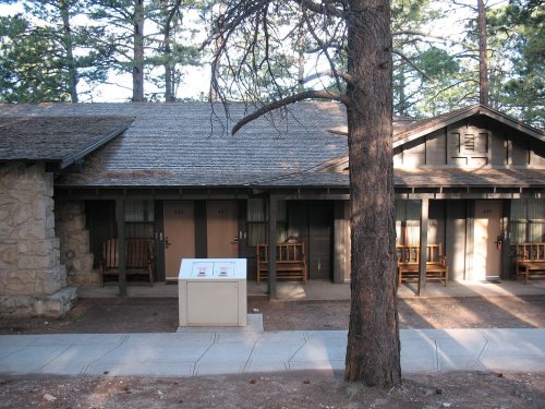 A rustic cabin with wooden benches outside, surrounded by trees and a concrete path leading to the entrance.