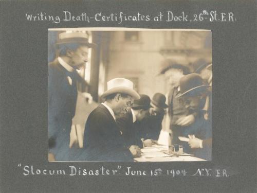 Historical photo of men writing death certificates at a dock, following the Slocum Disaster, June 15, 1904.