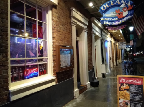 A nighttime view of Oceana Grill, featuring an open sign and menu specials outside a brick building.
