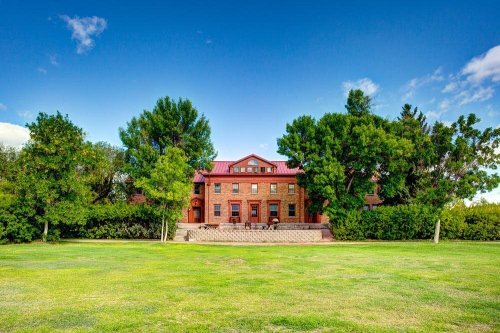 A large brick house with a red roof, surrounded by trees and a green lawn under a clear blue sky.