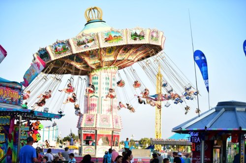 A colorful swing ride at a fair, with people enjoying the view against a clear blue sky.