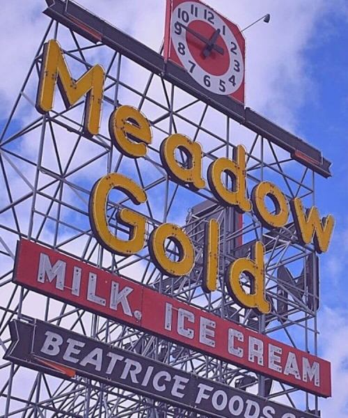 Vintage Meadow Gold sign featuring "Milk" and "Ice Cream" with a clock on top against a blue sky.