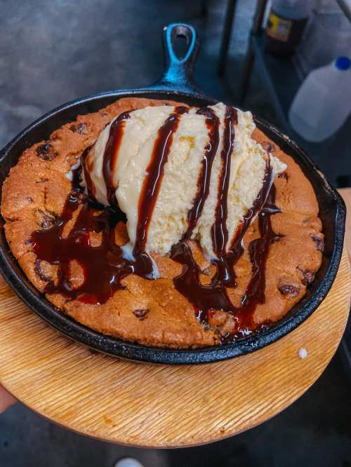 A warm chocolate chip cookie in a skillet, topped with vanilla ice cream and drizzled with chocolate sauce.
