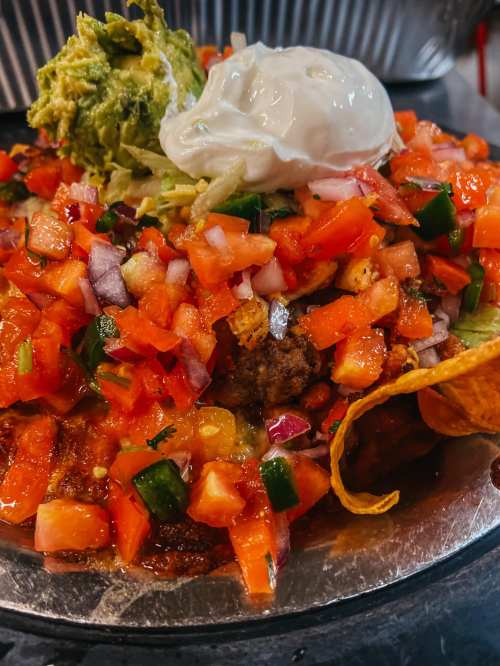 A colorful plate of nachos topped with guacamole, sour cream, diced tomatoes, onions, and seasoned meat.