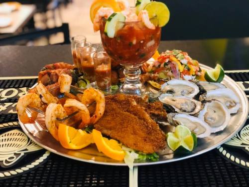 A seafood platter featuring shrimp, oysters, fish, and cocktails, garnished with lime and orange slices.