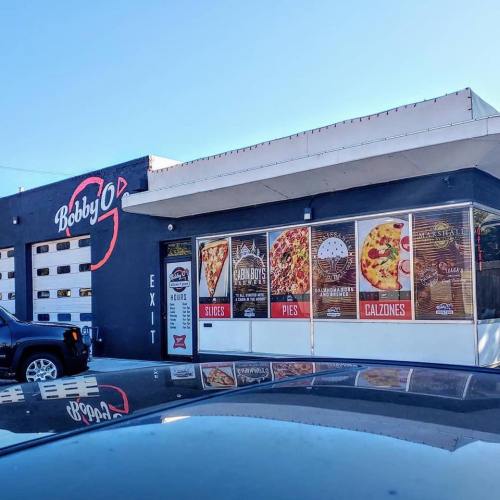 Exterior of Bobby O's restaurant featuring a menu display with slices, pies, and calzones. A car is parked nearby.
