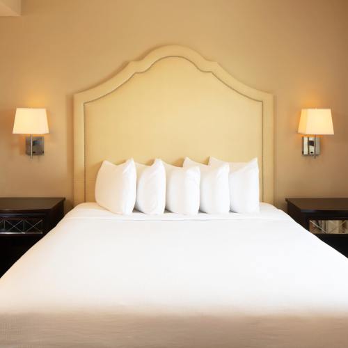 A cozy hotel room featuring a large bed with white pillows and soft lighting from wall sconces.