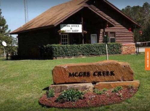 A wooden park office and gift shop building with a stone sign reading "McGee Creek" in front, surrounded by grass.