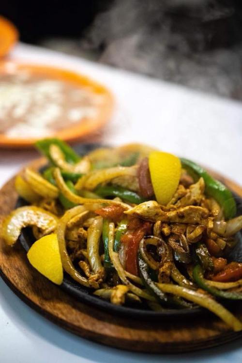 Sizzling chicken fajitas with bell peppers, onions, and lime wedges on a wooden platter.