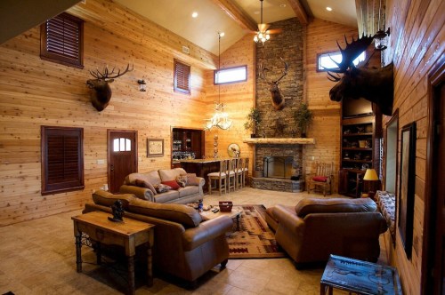 Cozy living room with wooden walls, stone fireplace, mounted deer heads, and comfortable seating.