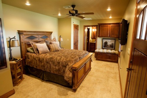 Cozy bedroom featuring a wooden bed, warm lighting, and a small seating area with a door leading to a bathroom.