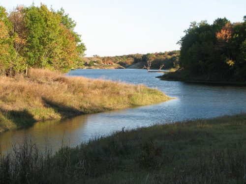 A serene river winding through lush greenery and golden grasses under a clear sky.