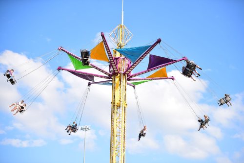 A colorful swing ride with passengers soaring against a blue sky and fluffy clouds.