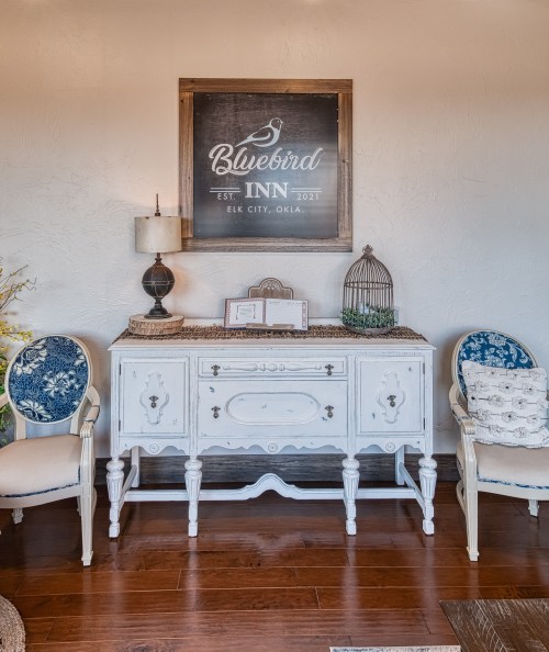 A vintage white sideboard with decorative chairs, featuring a sign for Bluebird Inn on the wall above.