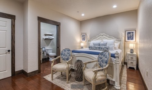 Cozy bedroom with a large bed, two chairs, and an adjoining bathroom, featuring warm lighting and elegant decor.