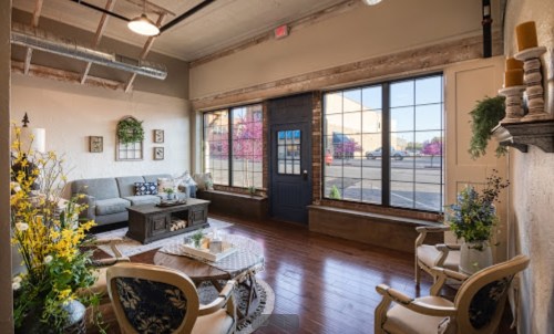 Cozy living room with a gray sofa, wooden accents, and large windows showcasing a vibrant outdoor view.