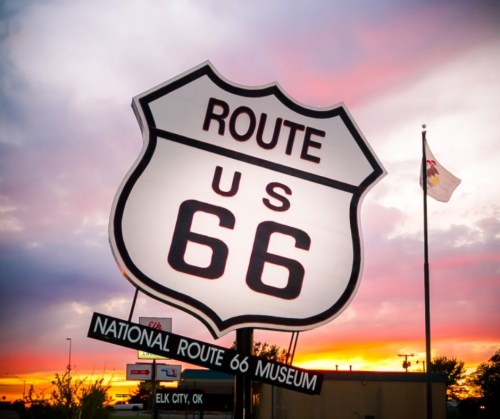 Sign for the National Route 66 Museum in Elk City, OK, with a colorful sunset in the background.
