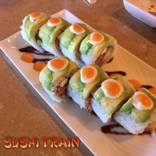 A plate of sushi rolls topped with avocado and orange sauce, served on a white dish with a drizzle of sauce.