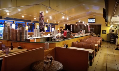 A cozy restaurant interior with booths, a long counter, and staff preparing food under warm lighting.