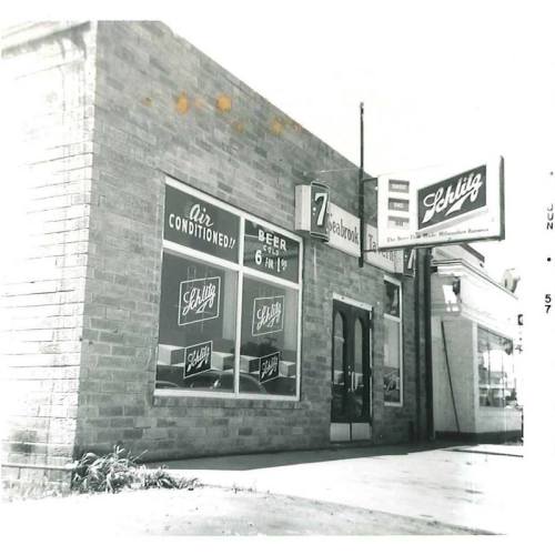 Black and white photo of a Schlitz beer storefront with signs for air conditioning and beer prices.