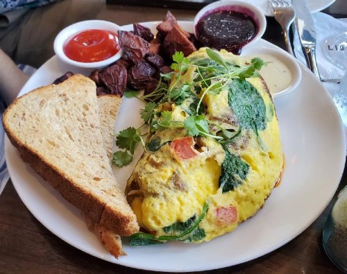 A plate with a vegetable omelette, toast, roasted potatoes, and sauces including ketchup and a berry compote.