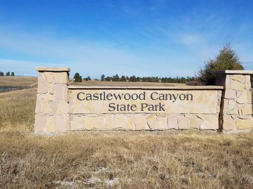 Sign for Castlewood Canyon State Park, featuring stone pillars and a clear blue sky in the background.