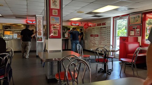 A casual diner interior with red booths, metal tables, and customers ordering at the counter.