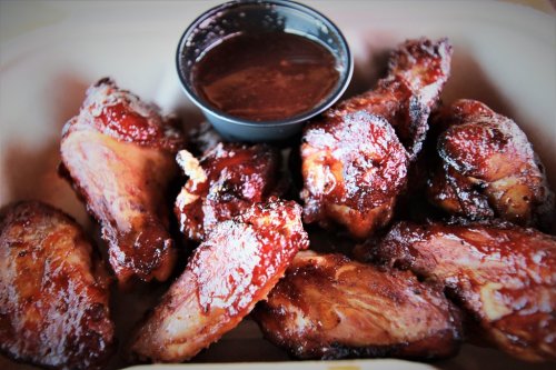 A plate of glazed chicken wings with a small cup of barbecue sauce on the side.