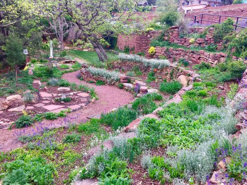 A lush garden with stone pathways, vibrant flowers, and greenery, set against a rocky hillside.