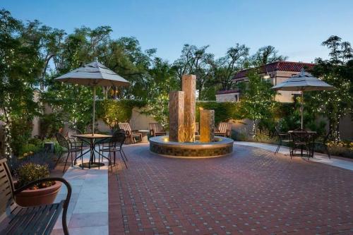 A serene outdoor courtyard with a fountain, surrounded by trees, tables, and string lights at dusk.