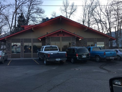 A building with a red roof and stone accents, surrounded by parked cars and bare trees.