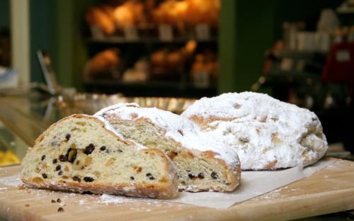 Sliced stollen bread dusted with powdered sugar, showcasing nuts and dried fruits, on a wooden cutting board.