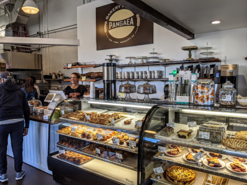A bakery display filled with pastries and desserts, with a barista serving customers at the counter.